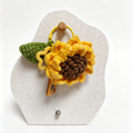 Knitted sunflower keychain on a white display stand with a white background