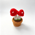 Crocheted red mushroom with white spots in a brown pot on a white background