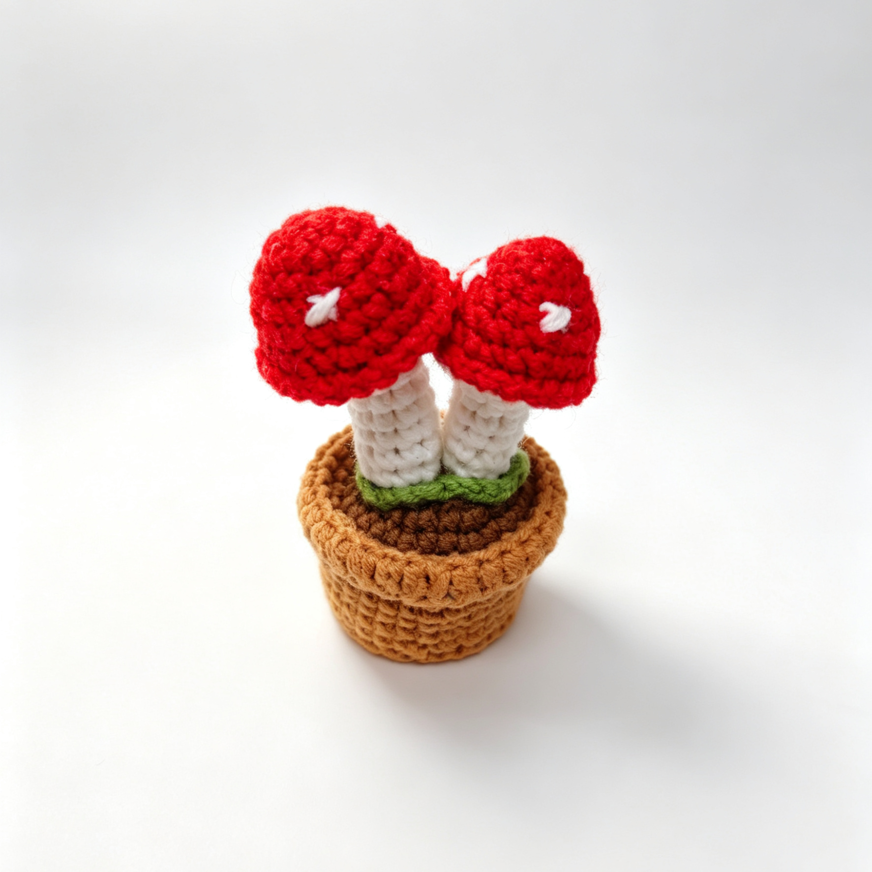 Crocheted red mushroom with white spots in a brown pot on a white background